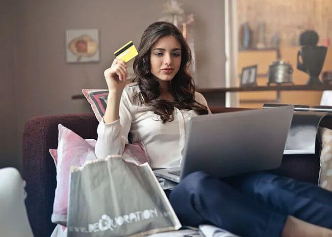 A woman sitting on a couch with a laptop and credit card.